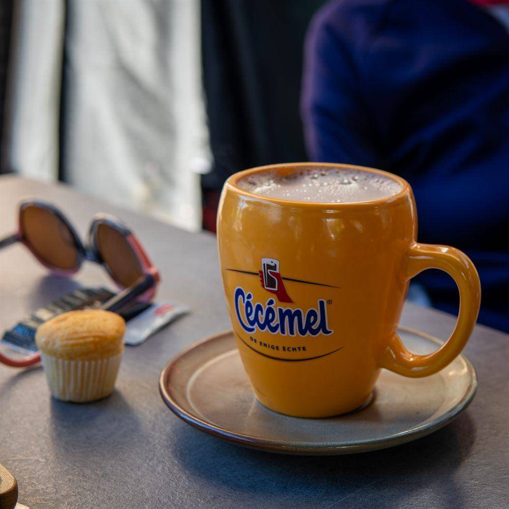 Een grote mok warme chocolademelk met een muffin ernaast op het terras.
