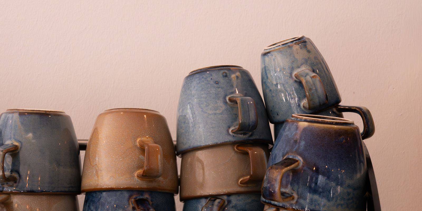 Gestapelde koffiekopjes in blauw en zandkleurig aardewerk op de koffiemachine.