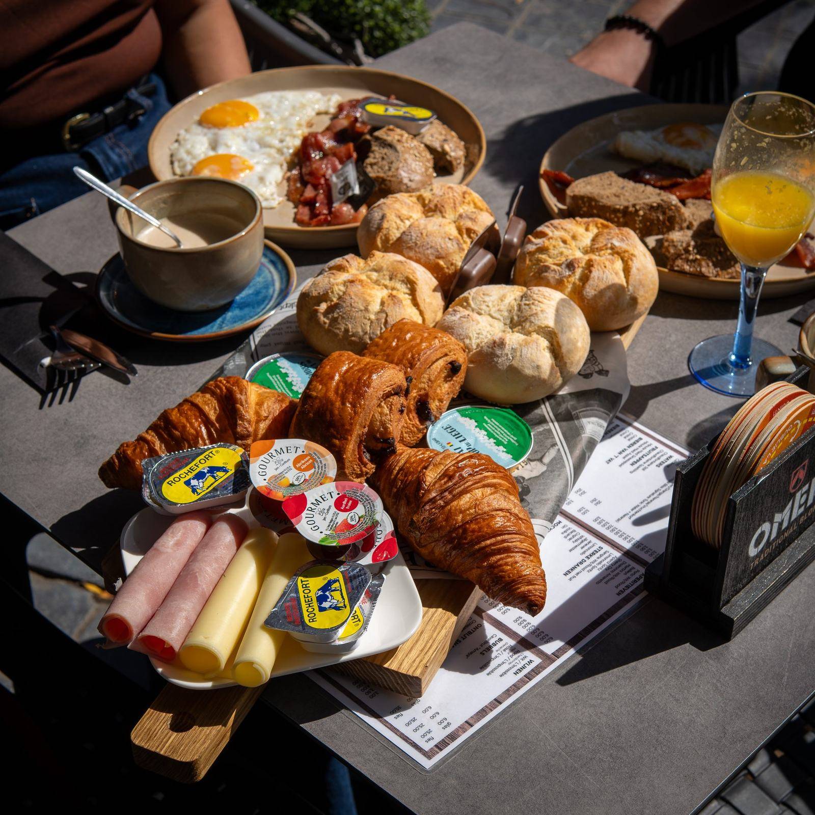 Een ontbijttafel met pistolets, croissants, spiegeleieren met spek, koffie en een glas cava.