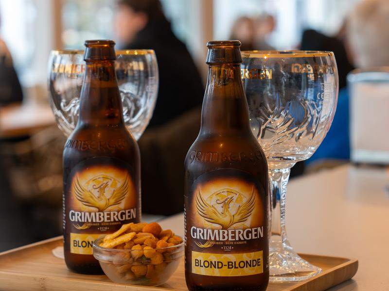 Twee flessen Grimbergen blond met glazen en nootjes.