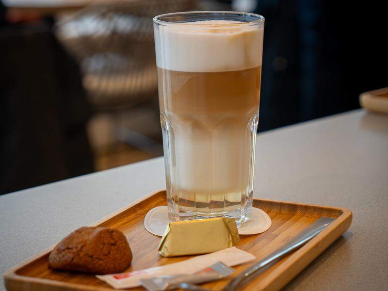 Een latte macchiato met een koekje op een houten plankje.