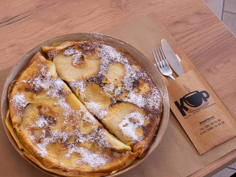 Een pannenkoek met gebakken appelschijfjes en poedersuiker.