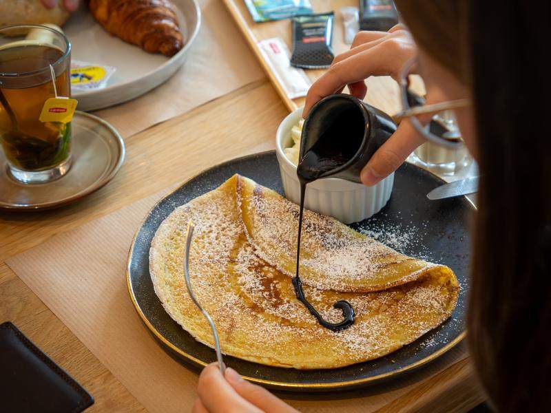Warme chocoladesaus wordt over een pannenkoek gegoten.