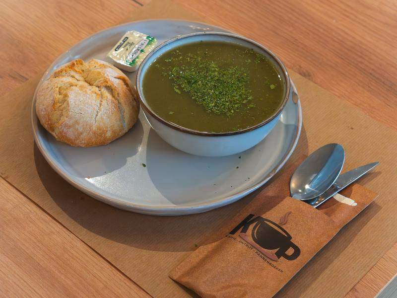 Een kom groene soep van de dag met een vers broodje.