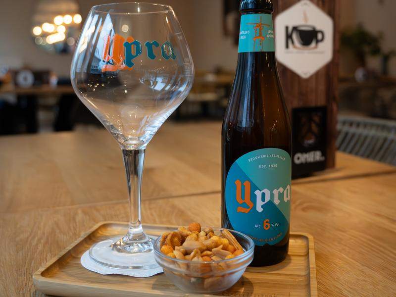 Een fles Ypra met glas en een bakje nootjes.