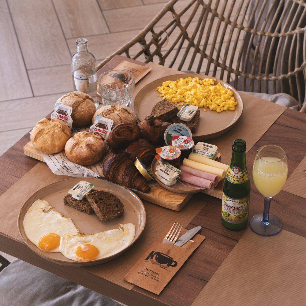 Ontbijttafel met broodjes, croissants, kaas, hesp, scrambled eggs en spiegeleieren.