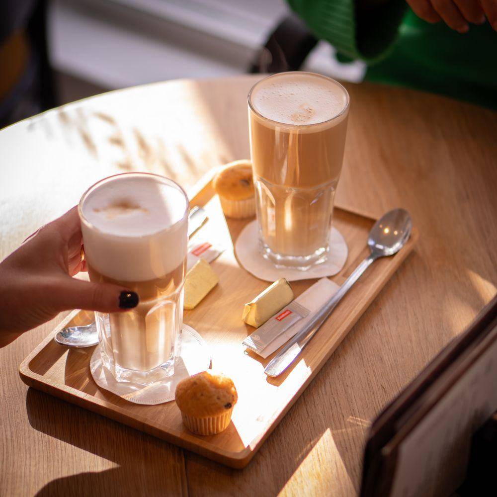 Een latte macchiato en een muffin op een houten dienblad in de zon.
