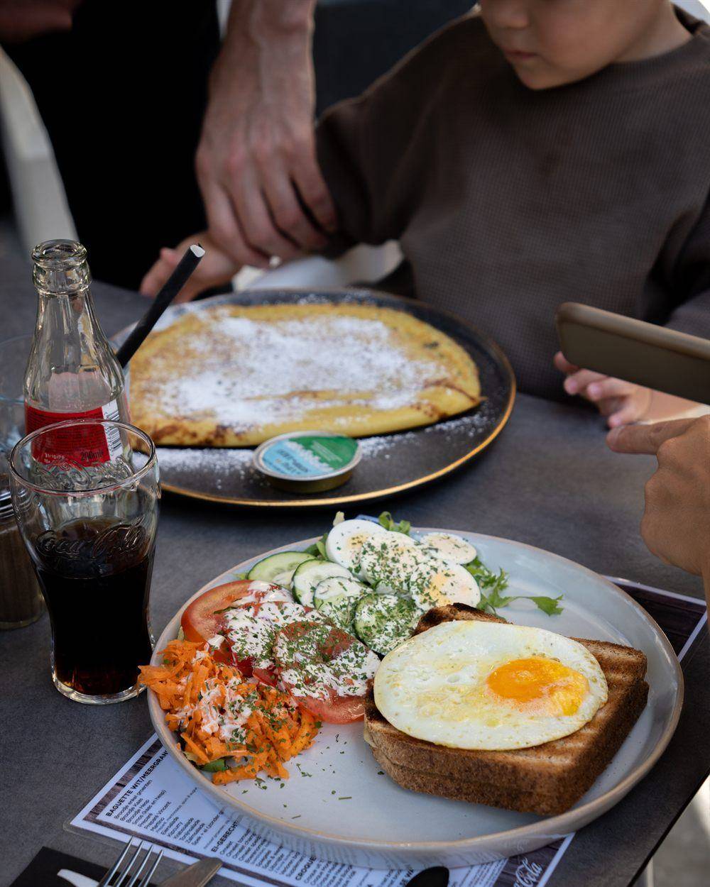 Een pannenkoek met poedersuiker en daarvoor een bord met spiegelei, toast en een frisse salade.