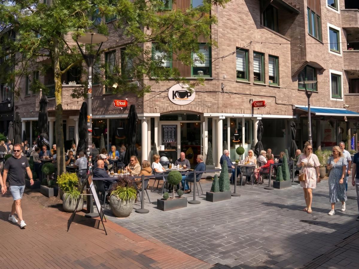De zaak van KOP op de hoek in de Stationsstraat, met een vol terras in de zon en voorbijgangers op straat.